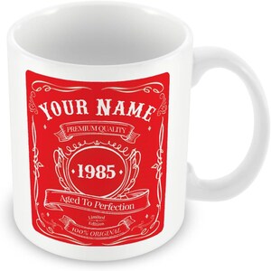 Pu&ograve; includere: Tazza in ceramica bianca con un design rosso. Il design presenta un'etichetta vintage con il testo "YOUR NAME", "PREMIUM QUALITY", "1985", "Aged To Perfection", "Limited Edition" e "100% ORIGINAL".