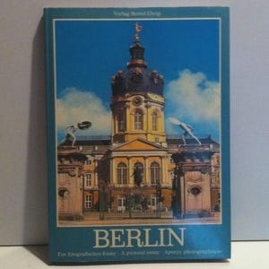 May include: A white ceramic mug with a black handle and the text "But First, Coffee" in a black, bold font. The mug is sitting on a wooden surface. The mug is 4 inches tall.