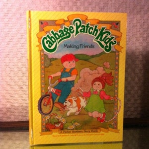 May include: A yellow book with the title "Cabbage Patch Kids Making Friends" and a picture of two children on a bicycle with a puppy. The book is a "Parker Brothers Story Book."