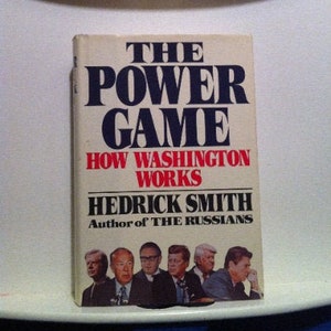 May include: A book titled "The Power Game: How Washington Works" by Hedrick Smith, author of "The Russians". The book cover features a group of men in suits.