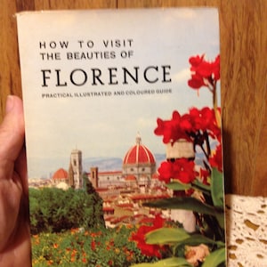 May include: A vintage travel guide book with the title "How to Visit the Beauties of Florence" and a colorful image of the city skyline with red flowers in the foreground.
