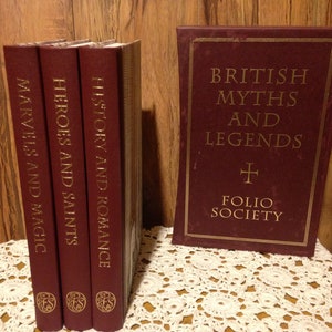 May include: A collection of burgundy-colored books with gold lettering. Titles include "British Myths and Legends" and "Marvels and Magic." The Folio Society logo is visible. The books are displayed on a white lace tablecloth.