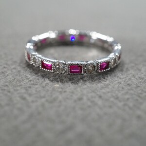 May include: A silver band ring with a row of alternating ruby and diamond stones.