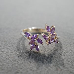 May include: A silver ring with two branches of purple amethyst stones.