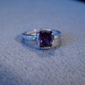 May include: A silver ring with a purple gemstone and small clear stones set in the band.
