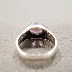 May include: A silver ring with a purple gemstone set in the center. The ring has a textured band.