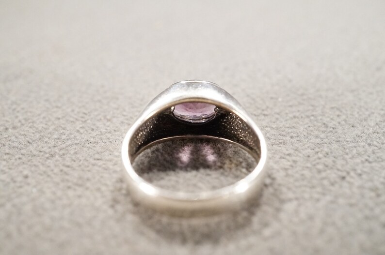 May include: A silver ring with a purple gemstone set in the center. The ring has a textured band.