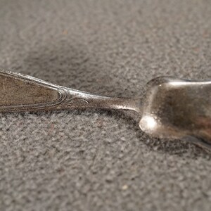 May include: A silver sugar spoon with an ornate handle and a scoop-shaped bowl.