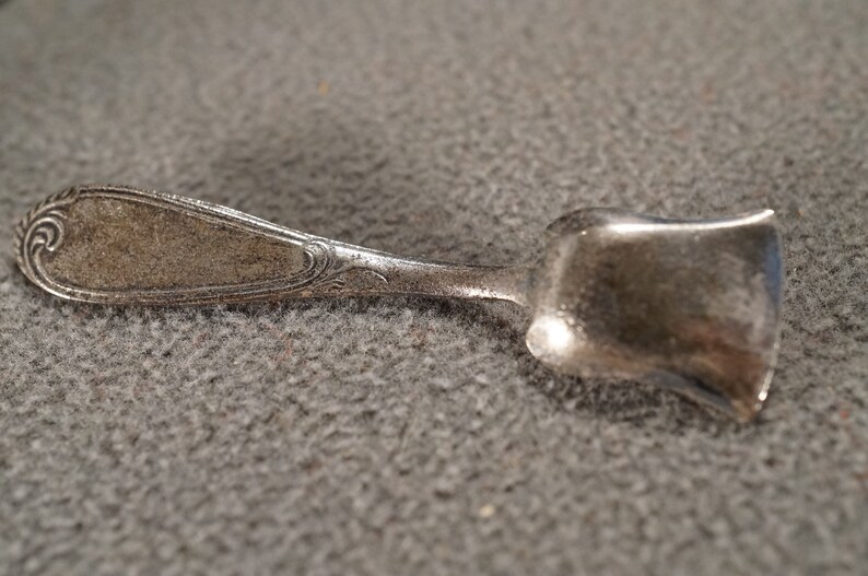 May include: A silver sugar spoon with an ornate handle and a scoop-shaped bowl.