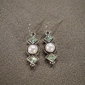 May include: Silver dangle earrings with a white pearl and green crystal accents.