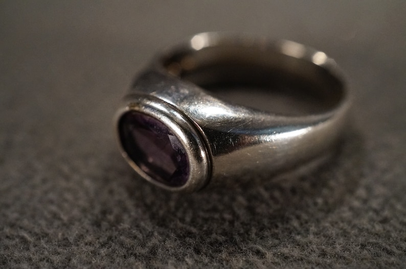May include: A silver ring with a bezel setting featuring a purple gemstone.