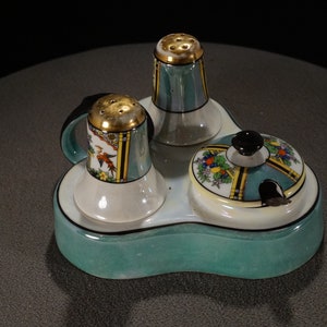 May include: A teal ceramic salt and pepper shaker set with a matching teal ceramic tray. The shakers have gold accents and floral designs. The tray has a black rim and a floral design.