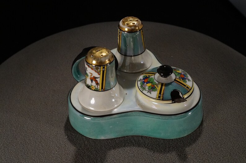 May include: A teal ceramic salt and pepper shaker set with a matching teal ceramic tray. The shakers have gold accents and floral designs. The tray has a black rim and a floral design.
