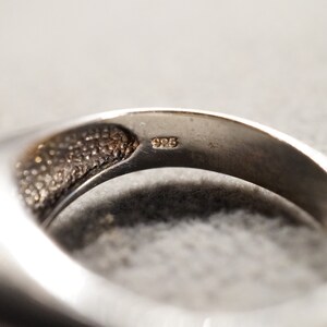 May include: Close-up of the inside of a silver ring with the inscription "925" on the band.