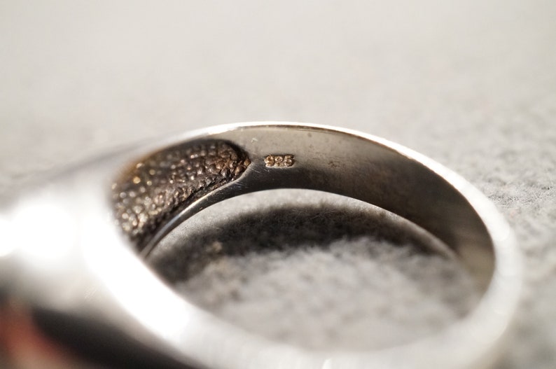 May include: Close-up of the inside of a silver ring with the inscription "925" on the band.
