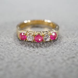 May include: A gold band ring with five red gemstones and four smaller clear gemstones.