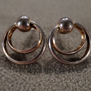 May include: A pair of silver earrings with a double circle design. The circles are connected by a small ball in the center.