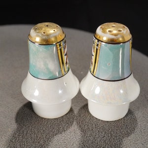 May include: Two salt and pepper shakers with a teal and gold design. The shakers have a white base and a gold rim.