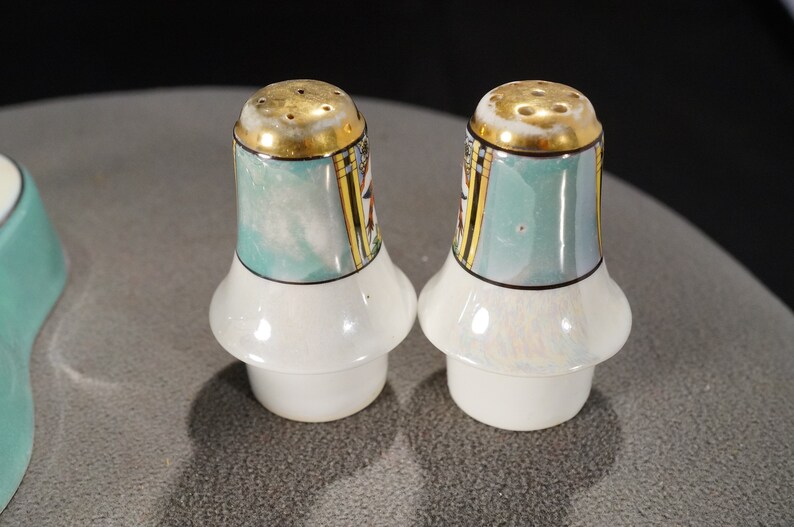 May include: Two salt and pepper shakers with a teal and gold design. The shakers have a white base and a gold rim.