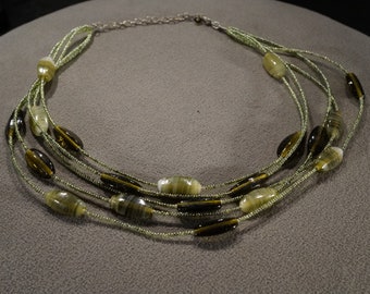 May include: A multi-strand necklace with green and brown oval beads. The necklace is made of small beads and has a silver clasp.