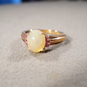 May include: A gold ring with a white opal gemstone and small pink gemstones set around the opal.