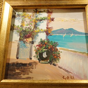 May include: A framed oil painting depicting a seaside scene with a view of a mountain range in the distance. The painting features two potted plants, a white building, and a blue sea with sailboats. The artist's signature, "Gozi", is visible in the lower right corner.