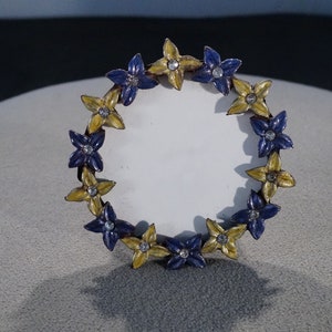 May include: A round picture frame with a white background and a border of alternating blue and yellow flowers with rhinestones in the center of each flower.