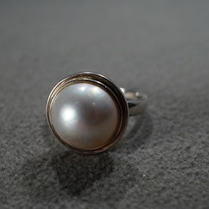 May include: A silver ring with a white pearl set in a circular bezel.