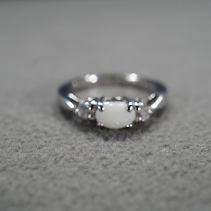 May include: A silver ring with a white oval opal gemstone and two smaller white gemstones on either side.