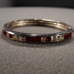 May include: A silver bangle bracelet with a band of red and clear rhinestones.