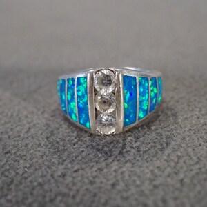 May include: A silver ring with blue opal and clear stones. The ring has a wide band with a curved top.