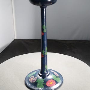 May include: A blue wooden hat stand with a round top and a base decorated with painted flowers. The flowers are red, pink, yellow, and green.