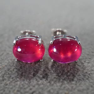 May include: A pair of silver earrings with oval-shaped red gemstones.