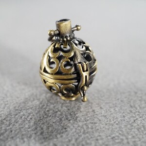 May include: A gold and silver metal cage pendant with an intricate design. The cage is open on one side and has a small loop at the top for hanging.
