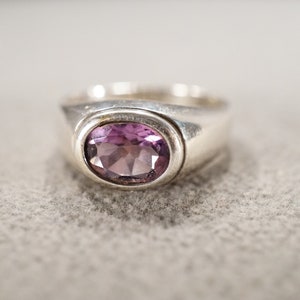 May include: A silver ring with a purple oval gemstone set in a bezel setting.