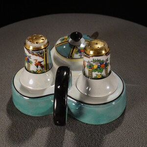 May include: A teal ceramic salt and pepper shaker set with a matching teal ceramic tray. The shakers have gold accents and floral designs. The tray has a black handle.