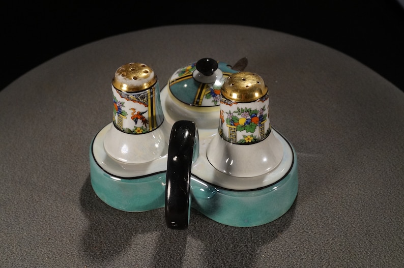 May include: A teal ceramic salt and pepper shaker set with a matching teal ceramic tray. The shakers have gold accents and floral designs. The tray has a black handle.