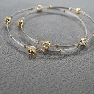 May include: Two silver and gold bracelets with small square-shaped charms. The charms have a clear crystal in the center.