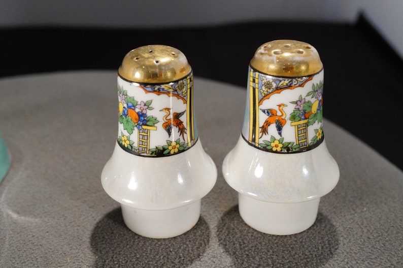 May include: A pair of white ceramic salt and pepper shakers with a gold top and a colourful floral and bird design.