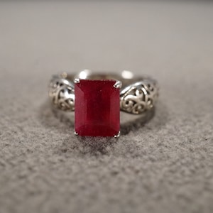 May include: A silver ring with an ornate filigree design and a large, rectangular, deep red ruby gemstone.