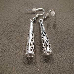 May include: A pair of silver dangle earrings with a delicate, intricate design. The earrings are made of metal and have a long, slender shape.