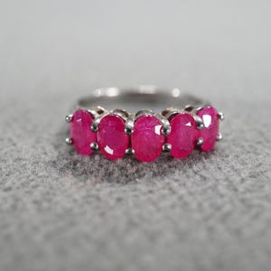 May include: A silver ring featuring five oval-cut, vibrant pink gemstones. The gemstones are set in a row across the top of the ring, creating a bold and eye-catching design. This piece of jewelry is suitable for everyday wear or special occasions.