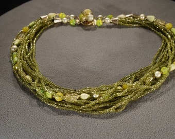 May include: A multi-strand necklace made of green glass beads with a silver clasp. The necklace features a variety of green beads, including some with a pearlescent finish.
