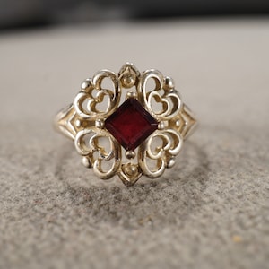 Puede incluir: Un anillo de plata con una piedra preciosa roja engastada en un diseño de filigrana.