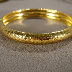 May include: A gold bangle bracelet with a hammered texture.