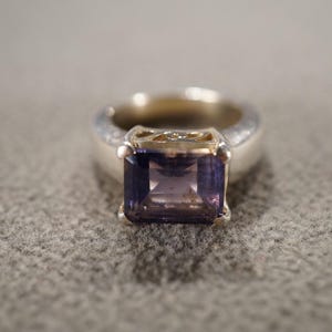 May include: A silver ring with a square-shaped purple gemstone.