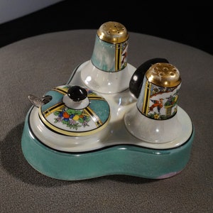 May include: A three-piece porcelain salt and pepper shaker set with a matching condiment dish. The set features a teal green base with a white rim and a black and gold design on the shakers and dish.