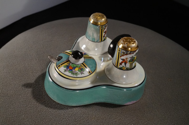May include: A three-piece porcelain salt and pepper shaker set with a matching condiment dish. The set features a teal green base with a white rim and a black and gold design on the shakers and dish.