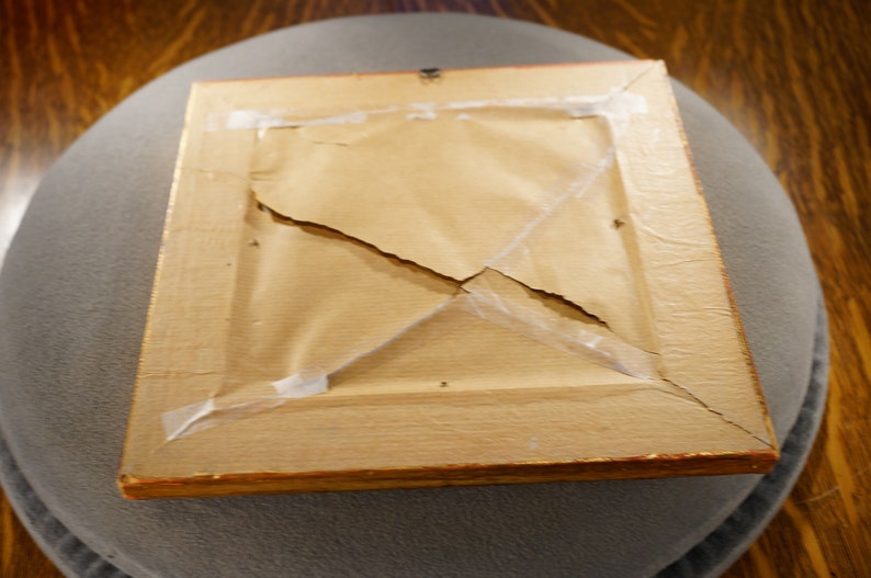 May include: The back of a wooden picture frame with a gold trim. The frame is cracked and has tape holding it together.