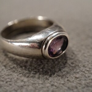 May include: A silver ring with a bezel setting featuring a purple amethyst gemstone.